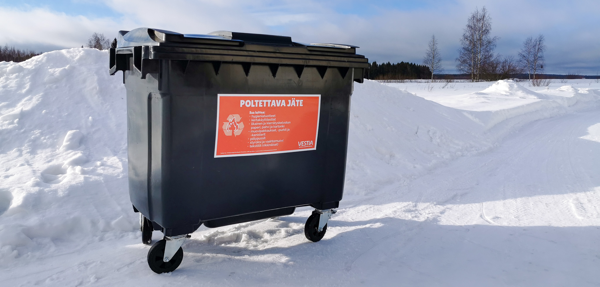 Poltettavan jätteen jäteastia talvisella pihalla. Taustalla paljon lunta ja taivasta.