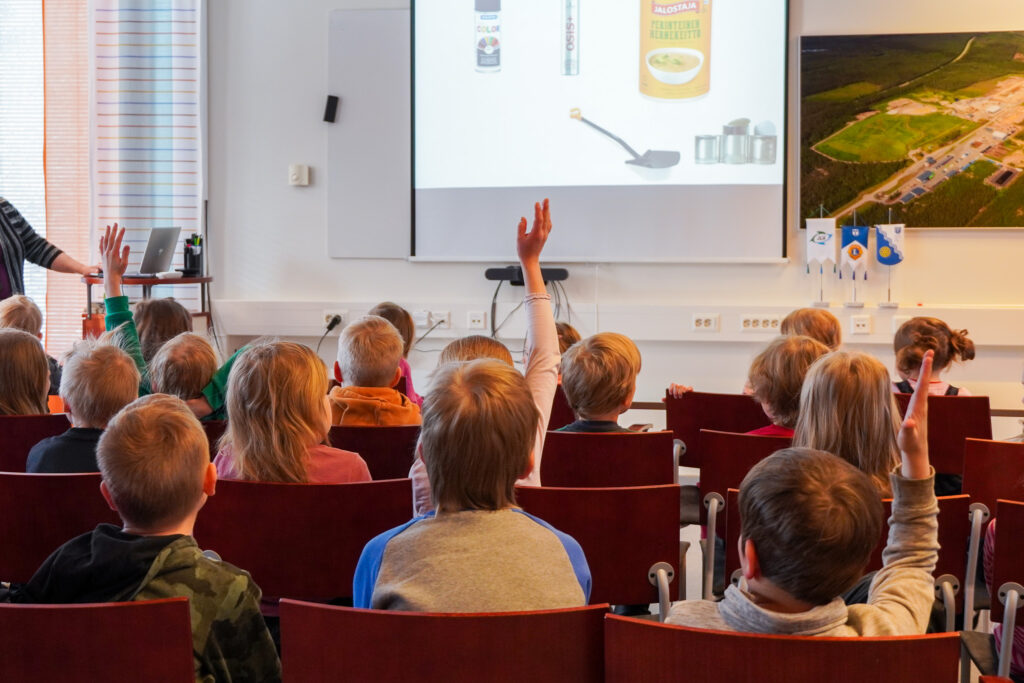 Alakouluikäisiä oppilaita Vestian kierrätysneuvontatilaisuudessa. Kuva otettu selkäpuolelta, yksi oppilaista viittaa.