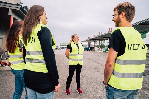 Neljä henkilöä heijastinliivit päällä Vestian kierrätysneuvontatilaisuudessa Ylivieskan lajittelupihalla.