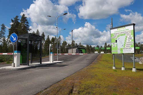 Oulaisten lajittelupihan sisääntulo. Kuvassa näkyy oikealla lajittelupihan karttakyltti, vasemmalla maksuautomaatti ja portti. Taustalla näkyy lajittelupihan rakennus ja puristimia.