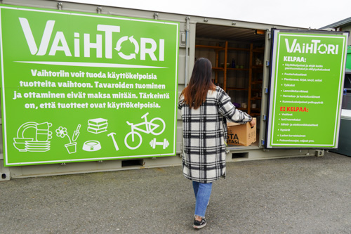 Henkilö kävelemässä Vaihtori-konttia kohti pahvilaatikko käsissään.