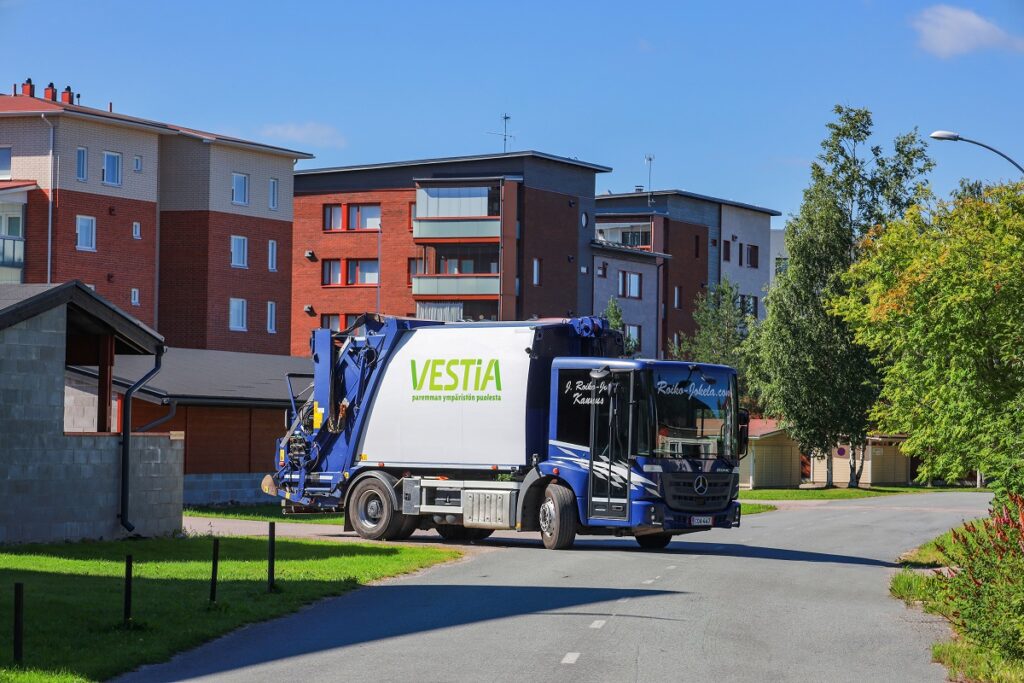 Vestian jäteauto kääntymässä taloyhtiön pihasta tielle. Taustalla näkyy kerrostaloja ja puita.