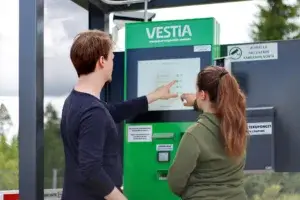 Kaksi henkilöä katsomassa ja osoittamassa Vestian lajittelupihan palveluautomaattia. Kuva otettu selkäpuolelta.